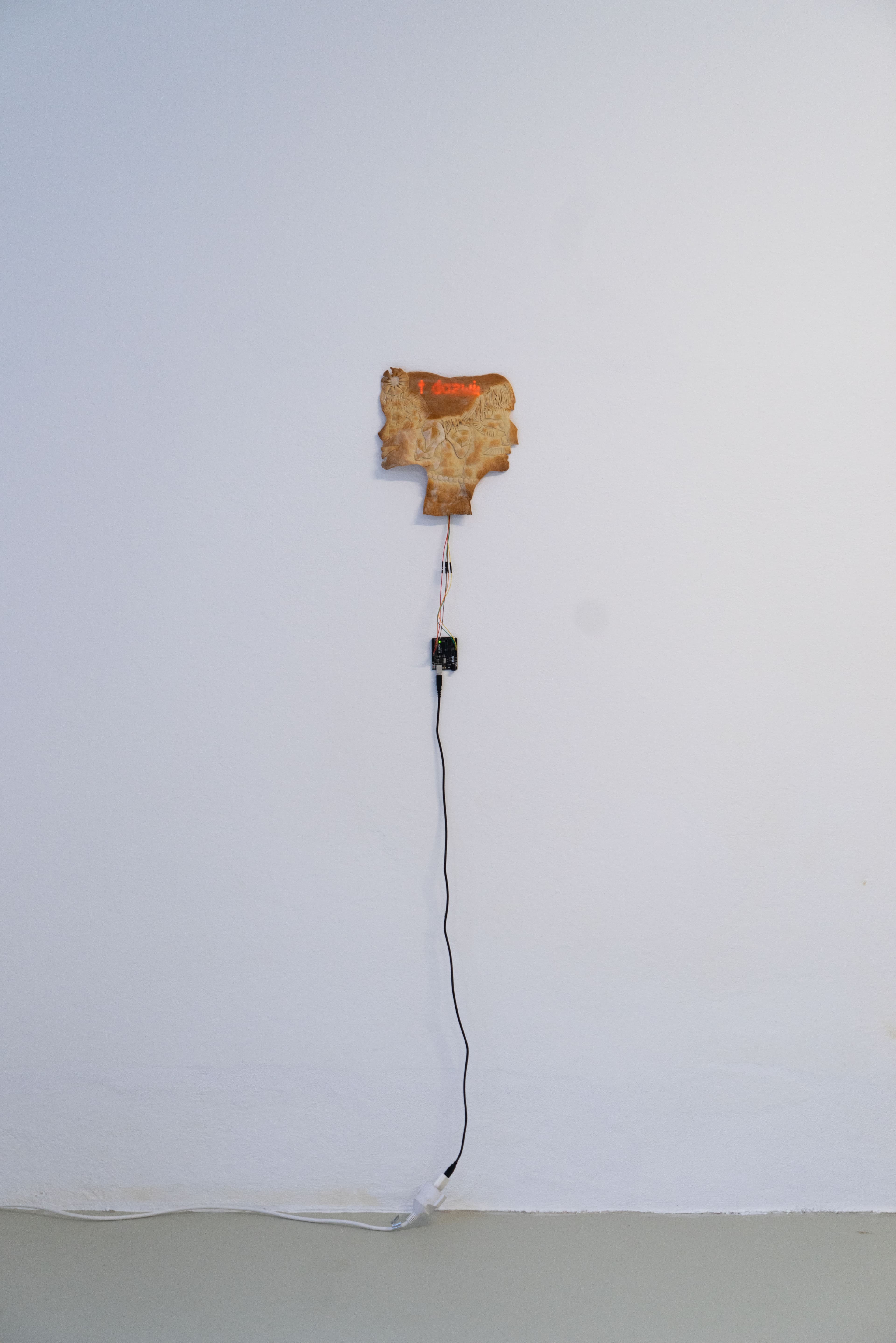 A double-faced mask made from bread, wires sticking out the bottom and a small LED panel that shines sentences through the thin layer of bread.