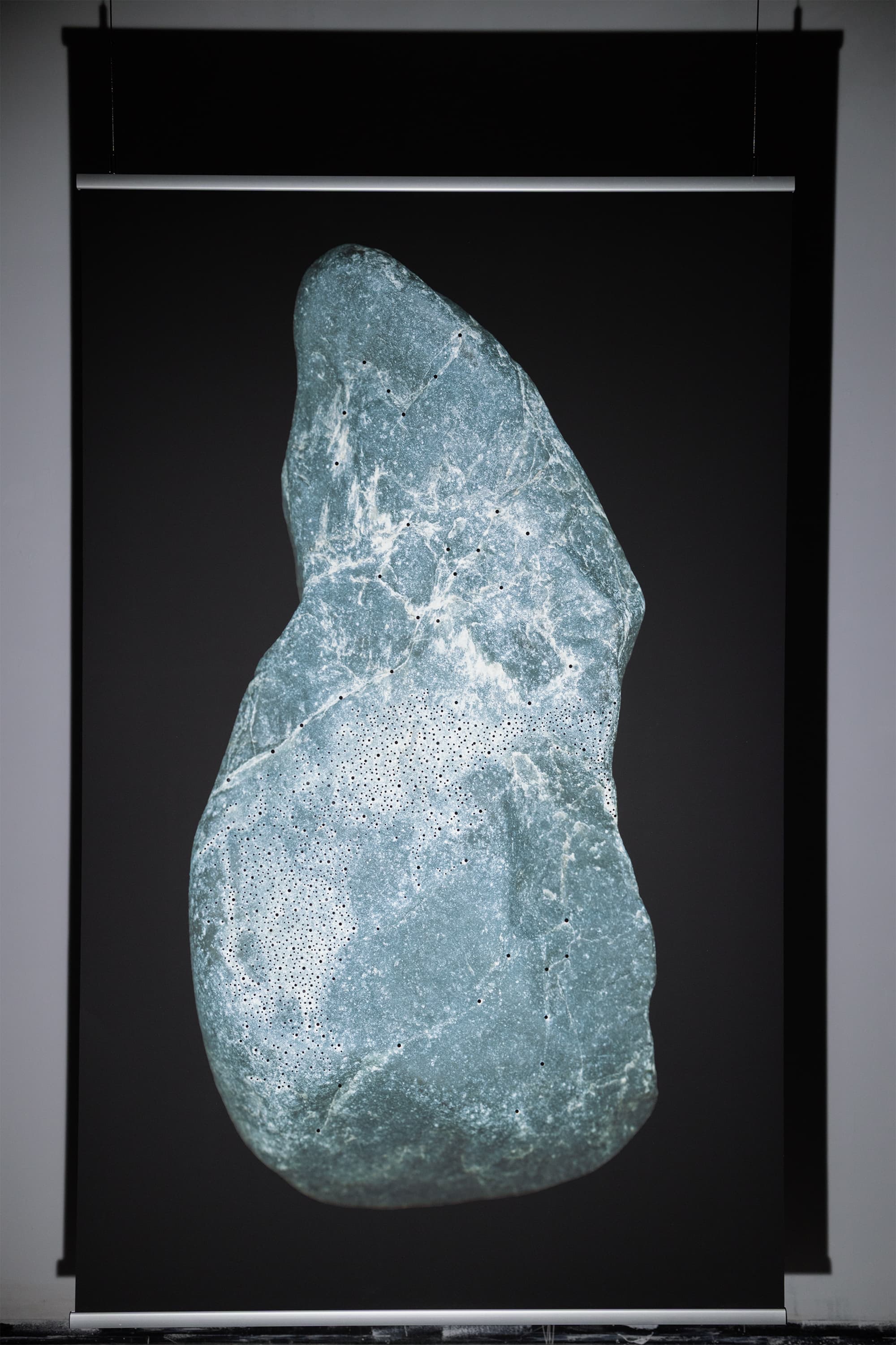The image is a high-resolution digital scan of the surface of a stone collected along the Dora River in Turin, Italy. Printed at a large scale, it amplifies the visual experience of the traces emerging from the rock. These figures are considered acheiropoietic images—forms not made by human hands.  The research draws on the practice of reading stones as a form of divination. The images revealed on the rock’s surface guide the divinatory act, activating the imagination and perceptual sensitivity of the seer.