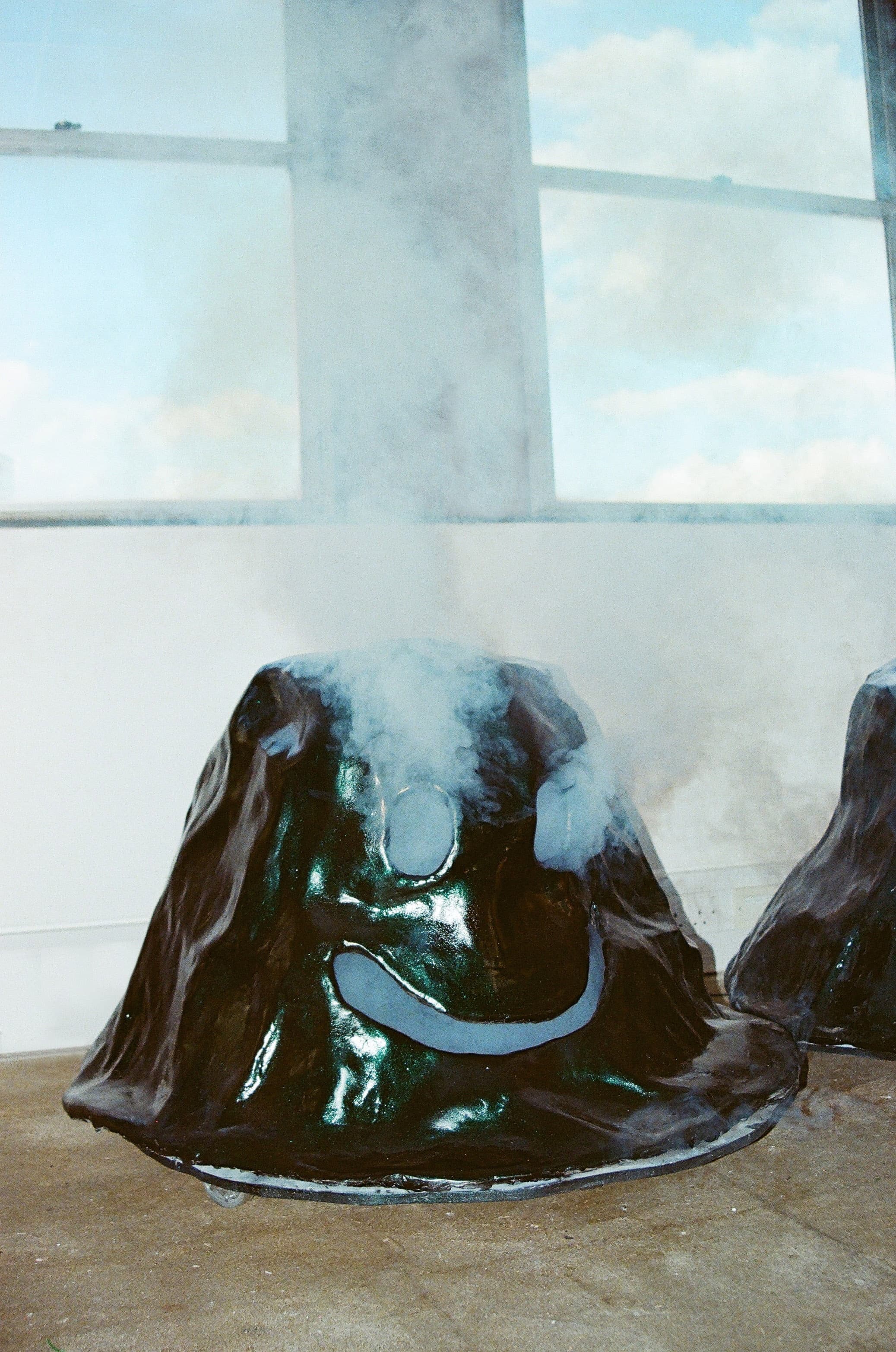 A dark ceramic object in the shape of a mountain with a smiley face emits steam.