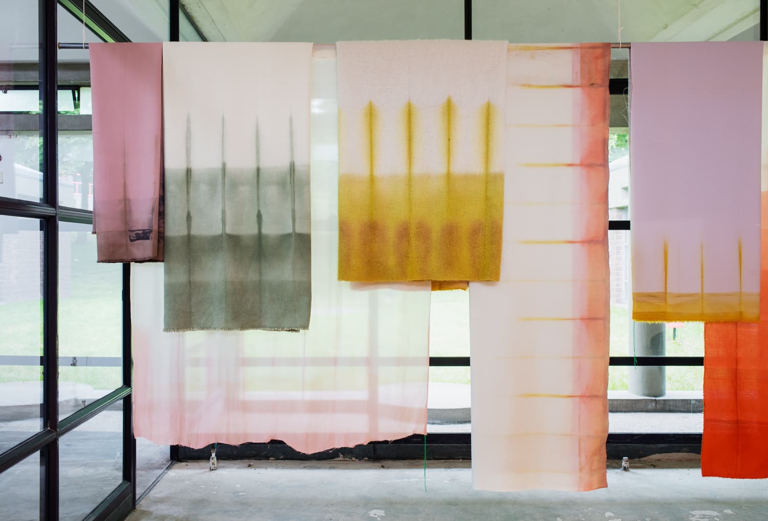 The image shows coloured/dyed fabrics hanging from a pole at the ceiling. 