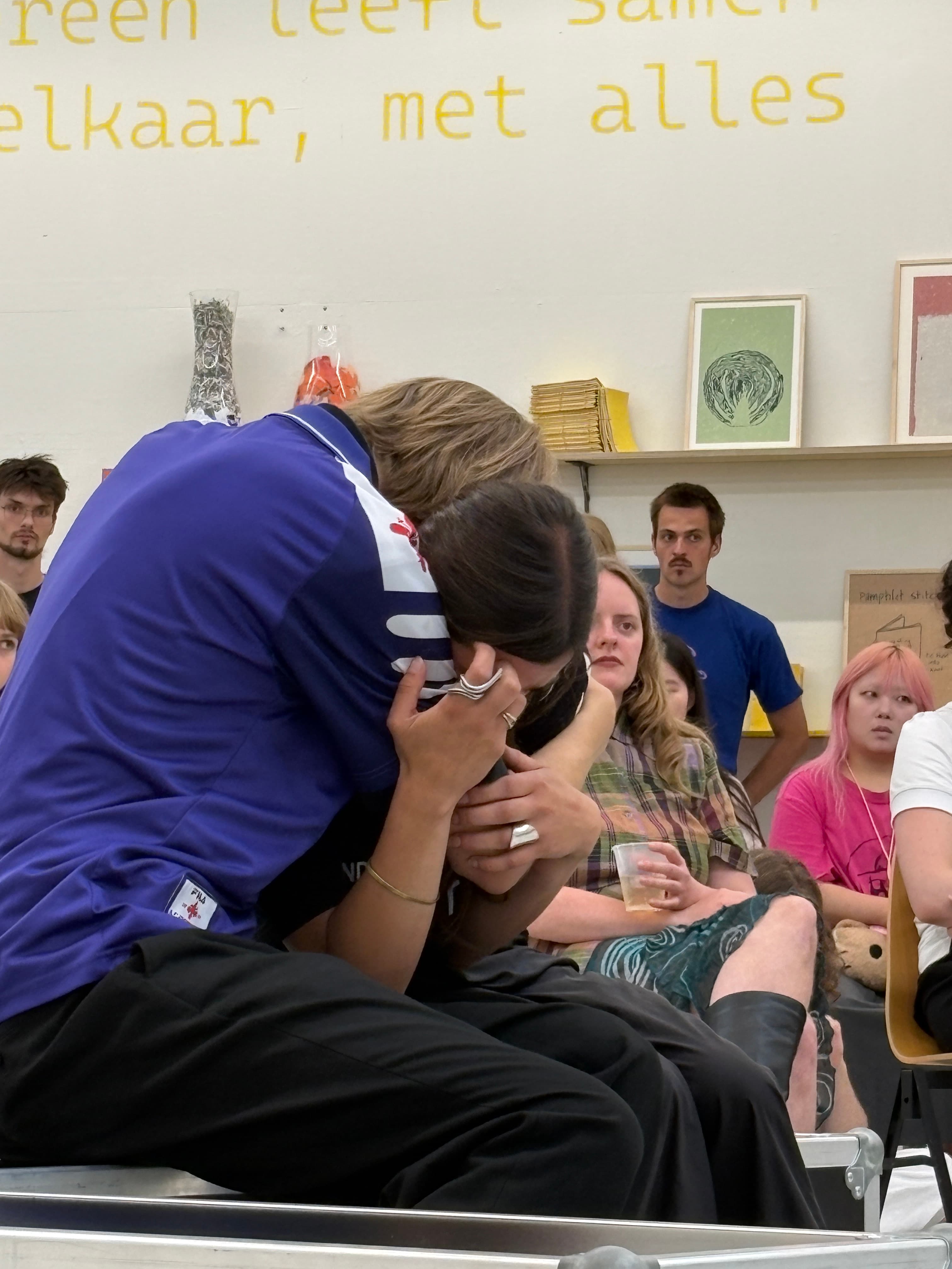 Two people hugging each other, public is sitting around them