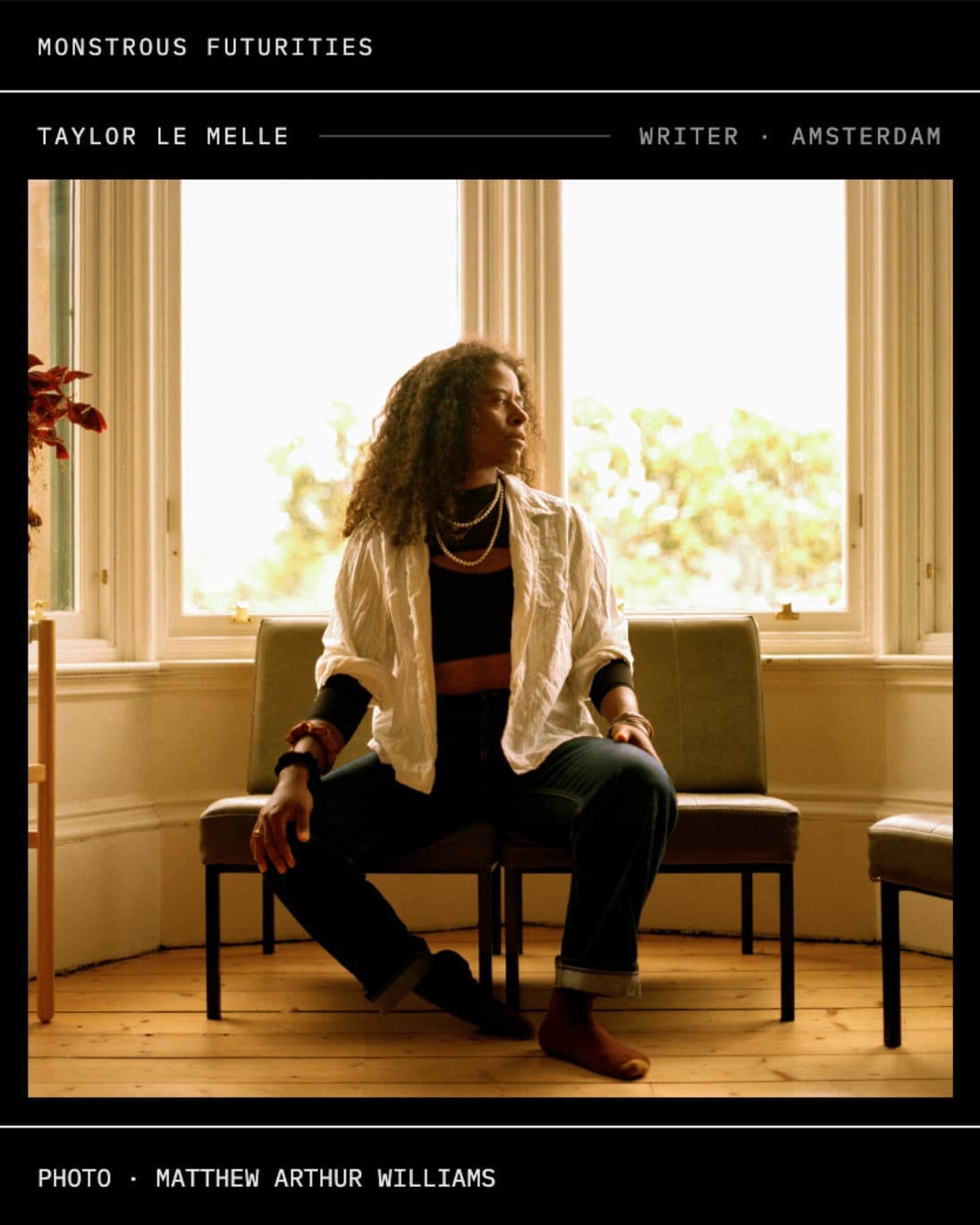 Image shows a woman sitting up right on a chair glancing to her left, in front of a bright window. She wears a loose white shirt over a crop top, and dark jeans, with no shoes.