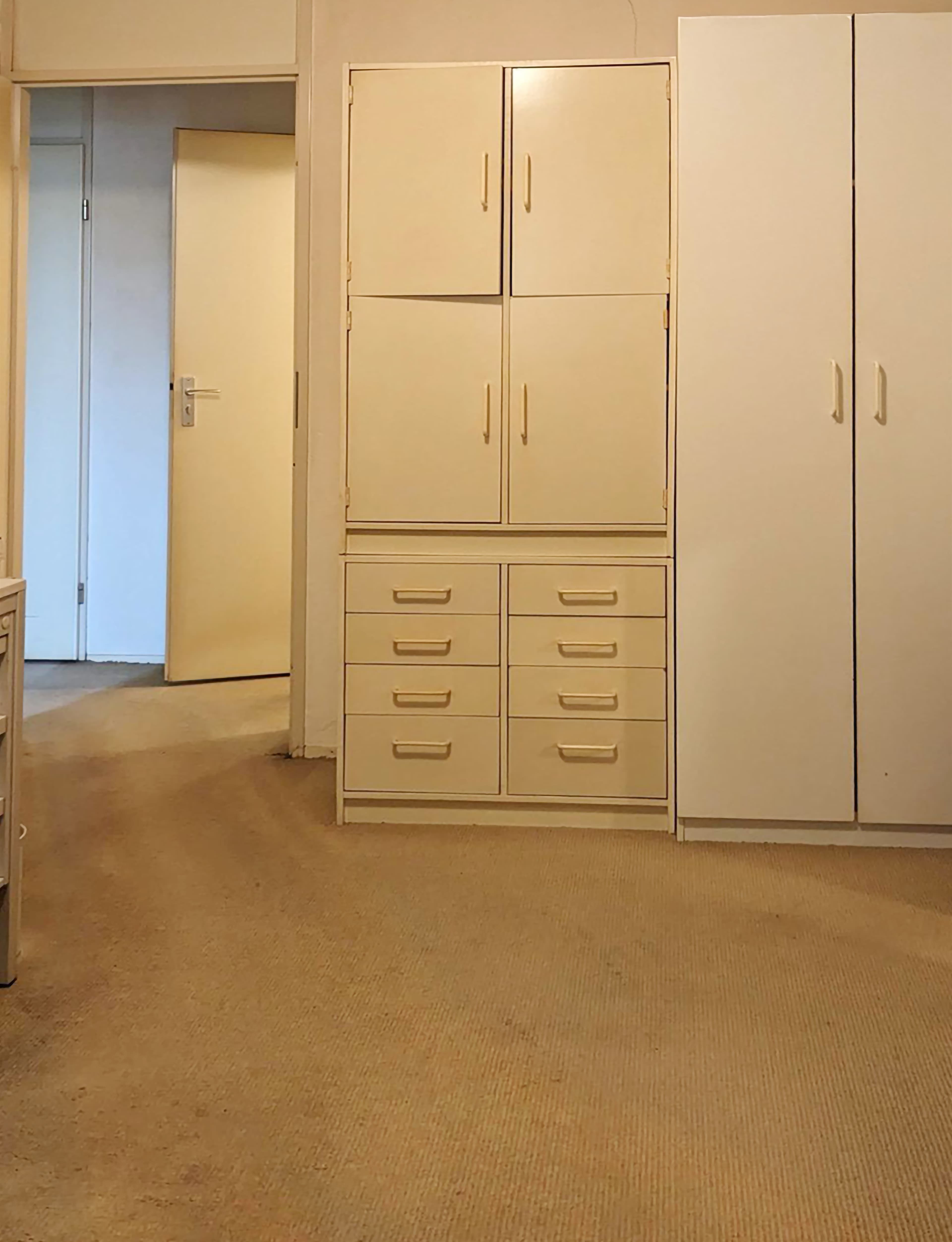 A plain, empty room with beige coloroud carpet and walls. The overall palette is very uniform and muted. 
