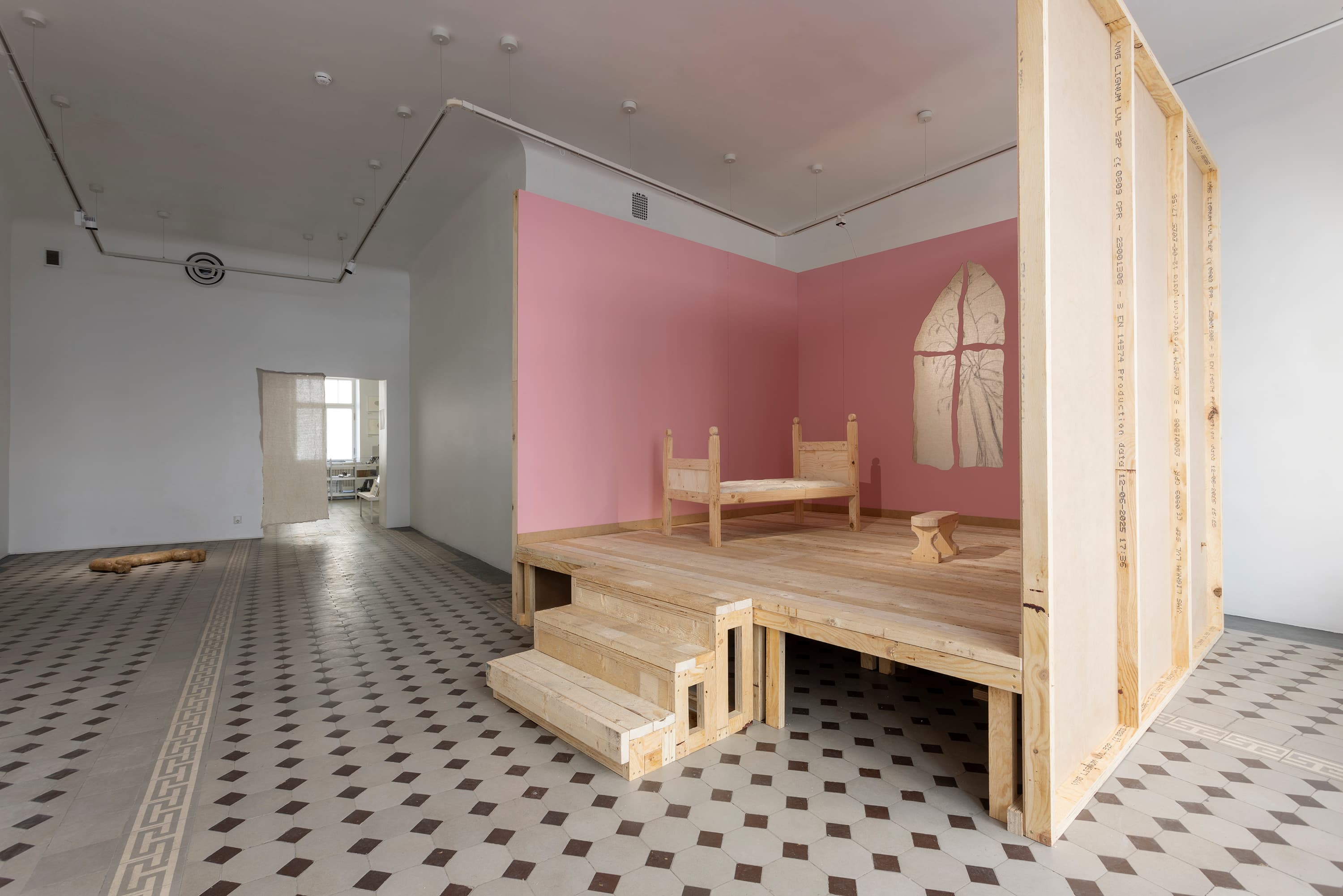 view to an exhibition space, showing a stage with pink walls constructed in one part of the room. further back, a sculpture is lying on the floor.