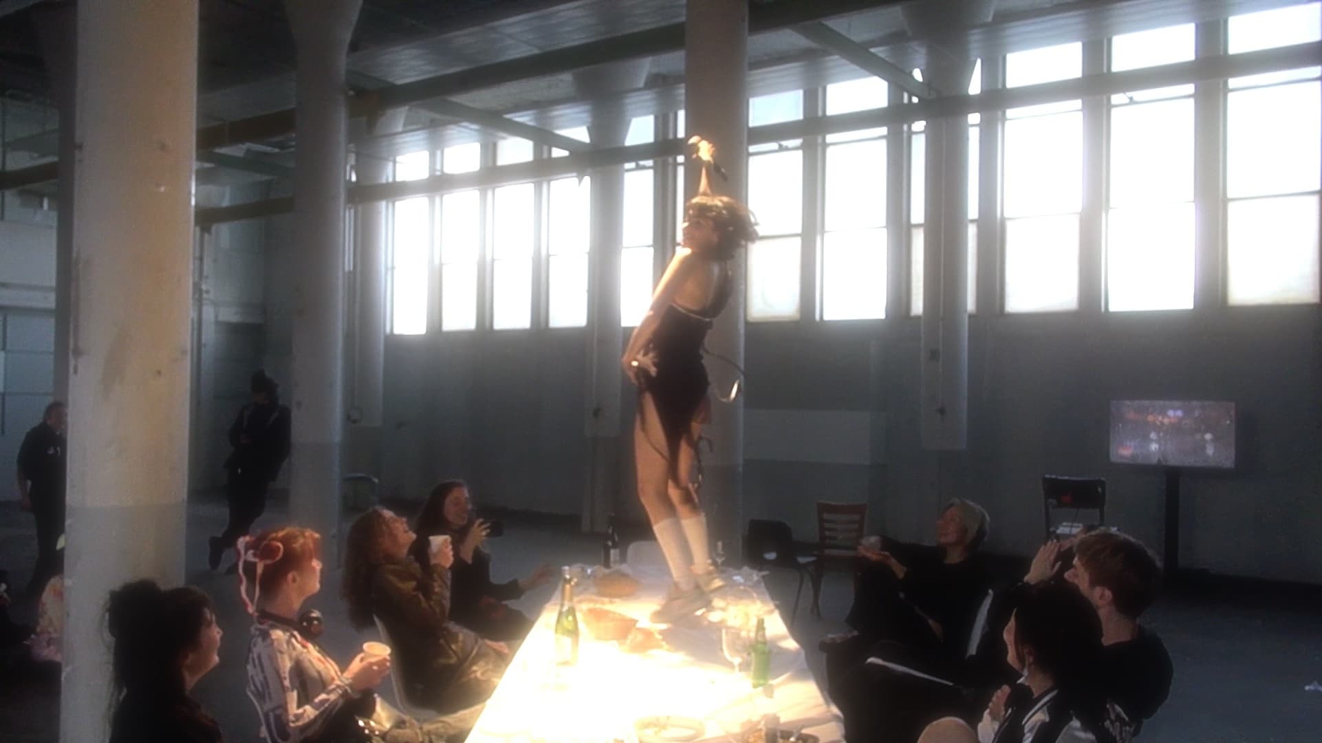 A woma dances on a table with people sitting around it.